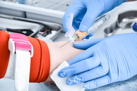 Healthcare professional wearing blue gloves inserts a needle into a patient's arm for a medical procedure.